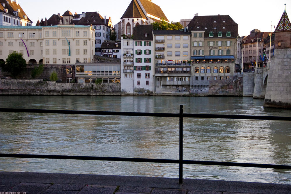 ﻿Basel. Mitten im Rhein sieht man hin und wieder die Köpfe schwimmender Leute. Kerstin erzählt, dass man weiter oben in der Stadt wasserdichte Plastiksäcke für die Kleider bekommt, so dass man bequem den Rhein herunter treiben kann. Unten angekommen zieht man sich dann die Kleider wieder an und fährt mit Bus oder Straßenbahn zurück in die Stadt.